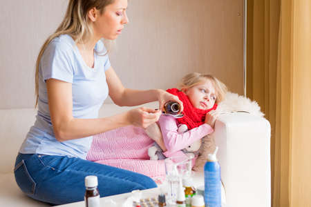 Mom giving syrup to her sick daughterの写真素材