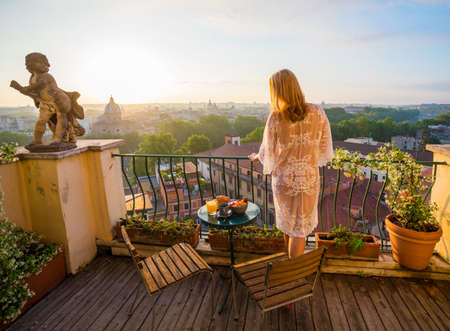 Woman standing on balcony and overlooking city in early morningの写真素材