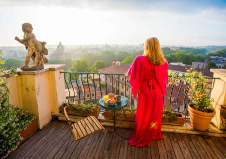 Woman standing on balcony and overlooking city in morningの写真素材