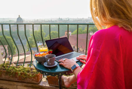 Woman using laptop during breakfast on balconyの写真素材