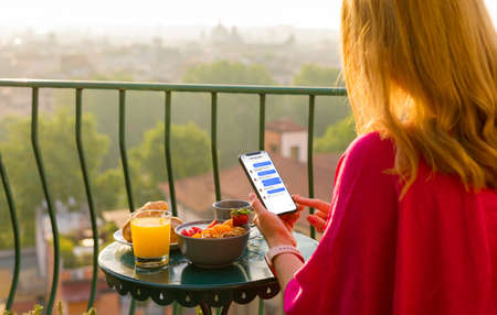 Woman chatting on phone at breakfast on terraceの写真素材