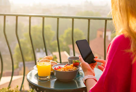 Woman using phone at breakfast on balconyの写真素材