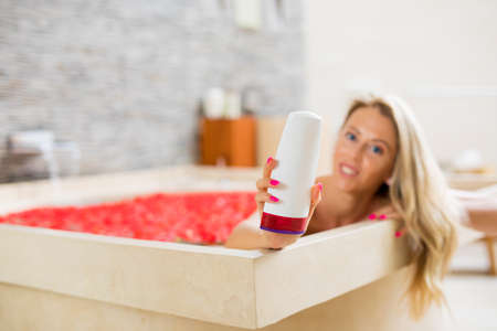 Woman in bath holding blank bathing product bottleの写真素材