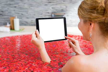Woman using tablet in red flower bathの写真素材
