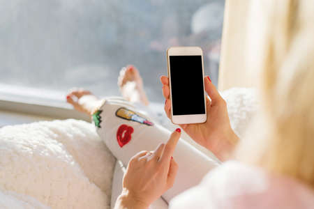 Woman holding phone while relaxing at homeの写真素材