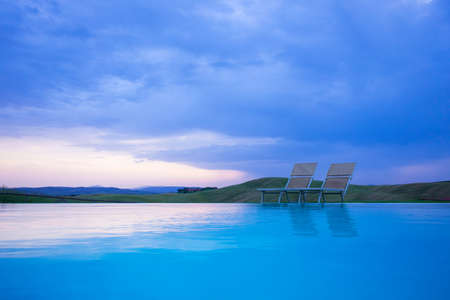 Swimming pool with two sun beds in evening light by sunsetの写真素材