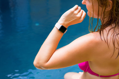 Woman wearing digital watch on hand by the pool