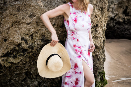 Woman in elegant summer dress and hat standing by the rocks