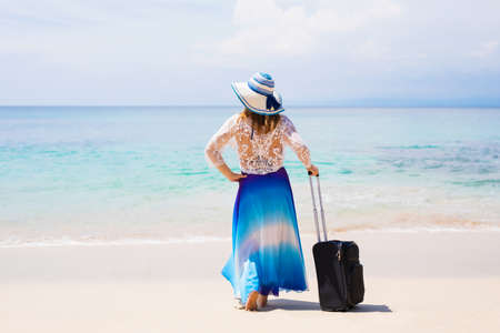 Woman with suitcase standing on exotic tropical beachの写真素材