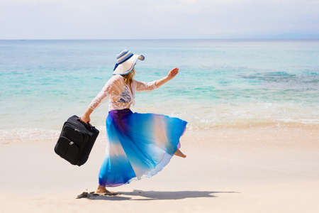Care free woman walking with suitcase on the beachの写真素材