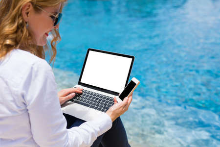 Woman using tech devices by the pool on vacationの写真素材