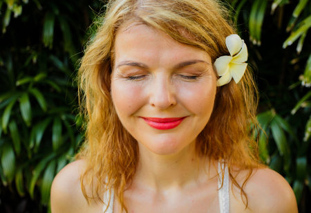 Woman with closed eyes in front of tropical green foliage. Vintage photo filter applied.