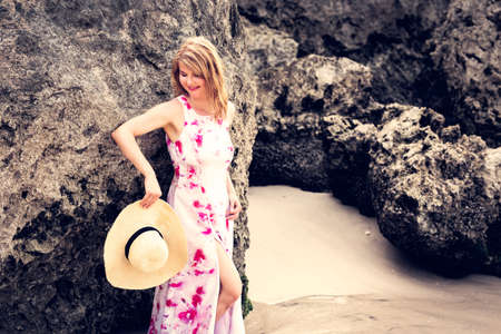Elegant woman standing by the rocks on the beachの写真素材