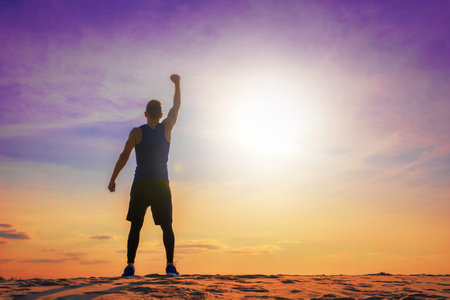 Fit and healthy man standing with raised hand, silhouette against colorful sky with sunlight.の写真素材