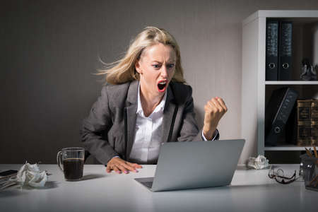 Woman angry at her laptop computer at workの写真素材