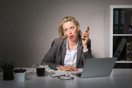 Tired woman having boring phone conversation at workの写真素材