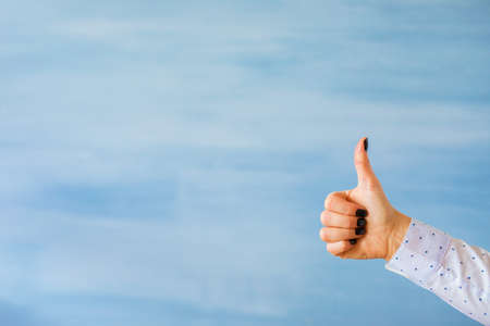 Person showing thumbs up hand gesture on empty blue backgroundの写真素材