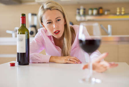 Woman reaching for a glass of wine while alone at homeの写真素材