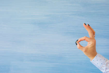 Person showing ok hand gesture on empty blue backgroundの写真素材