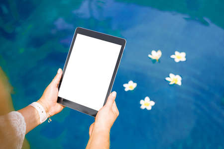 Woman sitting by the pool and using tablet computer. Vertical white screen .の写真素材
