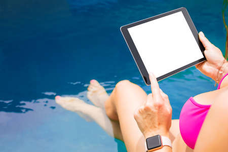 Woman sitting by the pool and using tablet computer. Horizontal screen orientation.の写真素材