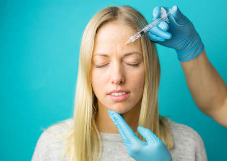 Doctor makes the rejuvenating facial injections for smoothing the face skin of a young womanの写真素材