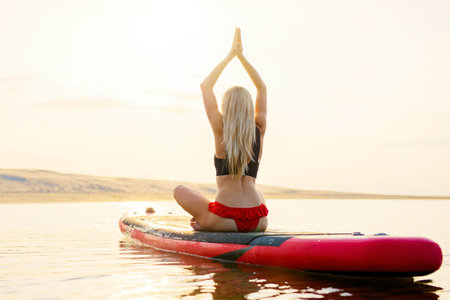 Fit woman doing yoga exercises on paddle board in the water at sunsetの写真素材