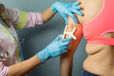 Dietitian doctor taking patient's body fat measurements on arm with fat caliperの写真素材