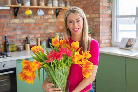 Woman holding colourful spring tulips in kitchenの写真素材