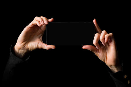 Person holding in both hands mobile phone horizontally, photo isolated on black backgroundの写真素材