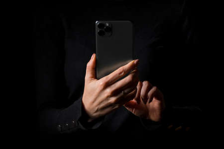 Person holding in hands mobile phone and touching screen with a finger, photo isolated on black backgroundの写真素材