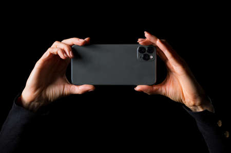 Person holding in hands and taking photo with mobile phone, photo isolated on black backgroundの写真素材