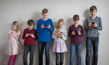 Children standing together in everyone using their own mobile phoneの写真素材