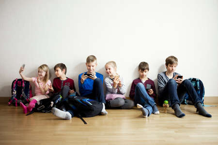 Smiling kids sitting on floor with mobile devicesの写真素材