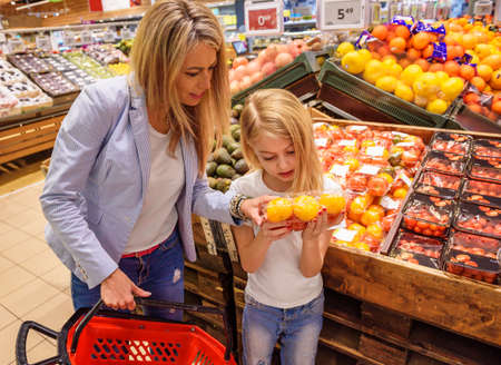 Mother and daughter buying ecologically grown fruits and vegetables in groceries storeの写真素材