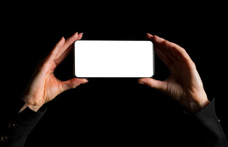 Person holding in hands mobile phone with blank screen and taking photo, image isolated on black backgroundの写真素材