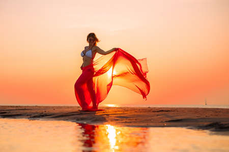 Woman posing with piece of clothing on the beach at sunsetの写真素材