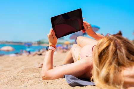 Woman using tablet while relaxing on the beach in hot summer dayの写真素材