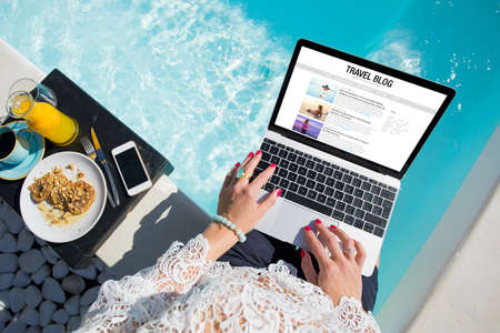 Woman working on her travel blog outdoors by the poolの写真素材