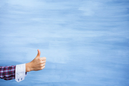 Girl showing hand with thumbs up gesture on clean painted backgroundの写真素材