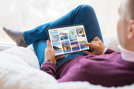 Man browsing beautiful winter photos on tablet at homeの写真素材