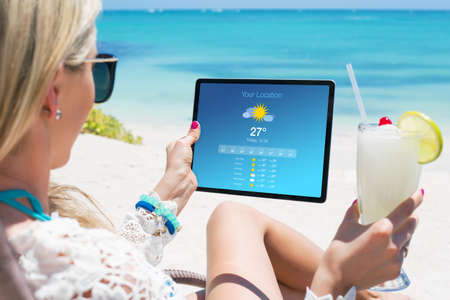 Woman viewing weather forecast on tablet while relaxing on the beachの写真素材