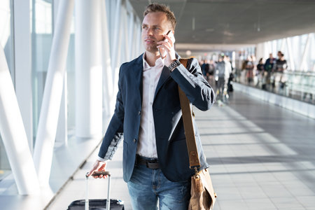 Young man walking through airport gate and talking on phoneの写真素材