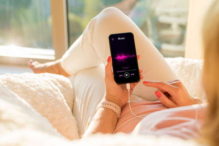 Woman listening to music on mobile phone while relaxing at homeの写真素材