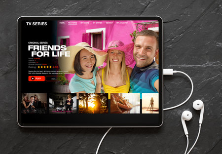 Tablet computer with earphones on black background showing movie and TV shows online streaming service app on the screenの写真素材