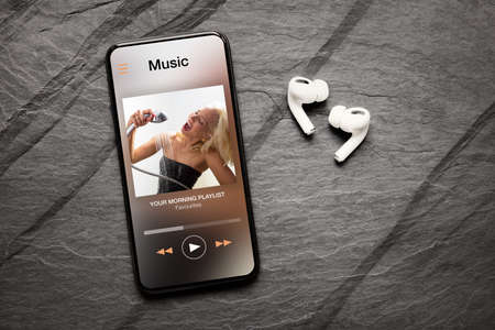 Music player on screen of mobile phone and wireless earphones on dark backgroundの写真素材