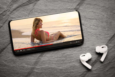 Video player on screen of mobile phone and wireless earphones on dark backgroundの写真素材