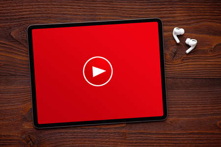 Play button on the screen of tablet and wireless earphones on dark wooden surfaceの写真素材