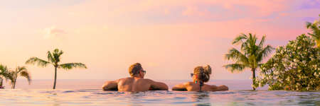 Panoramic photo of couple in pool enjoying tropical vacation by sunsetの写真素材