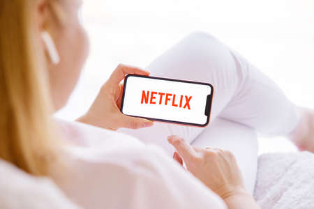 Riga, Latvia - March 26, 2021: Woman holding mobile phone with Netflix logo on the screenのeditorial素材